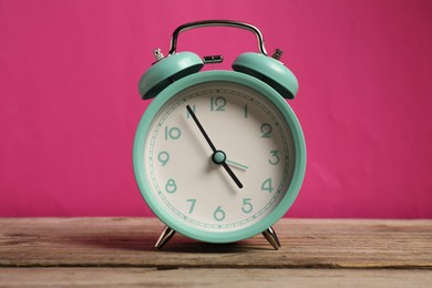 Photo of One turquoise alarm clock on wooden table against bright pink background