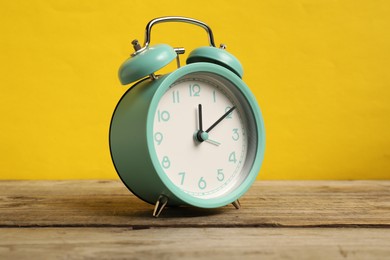 Photo of One turquoise alarm clock on wooden table against yellow background