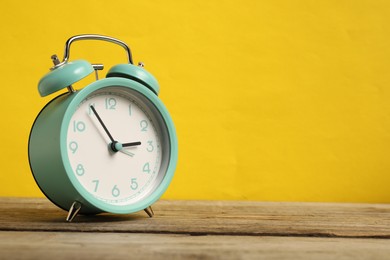 Photo of One turquoise alarm clock on wooden table against yellow background, space for text