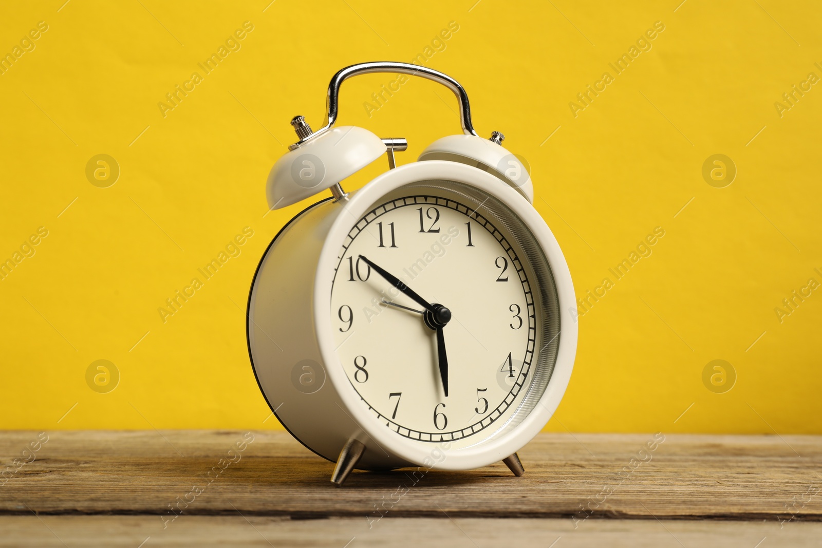 Photo of One white alarm clock on wooden table against yellow background