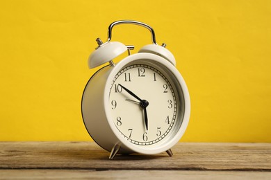 Photo of One white alarm clock on wooden table against yellow background