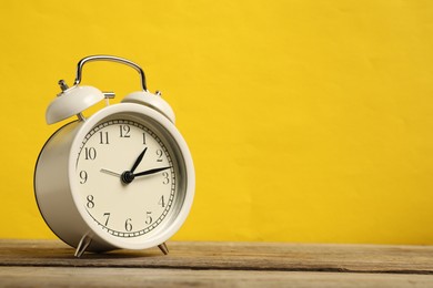 Photo of One white alarm clock on wooden table against yellow background, space for text