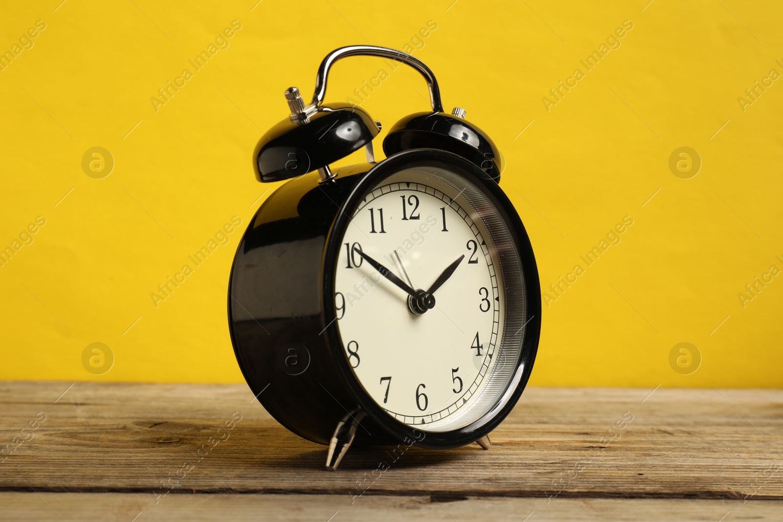 Photo of One black alarm clock on wooden table against yellow background