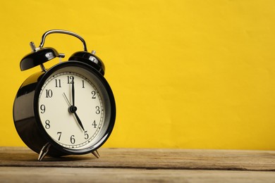 Photo of One black alarm clock on wooden table against yellow background, space for text