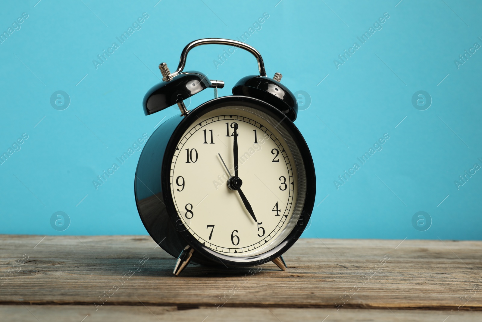 Photo of One black alarm clock on wooden table against light blue background