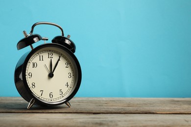 Photo of One black alarm clock on wooden table against light blue background, space for text