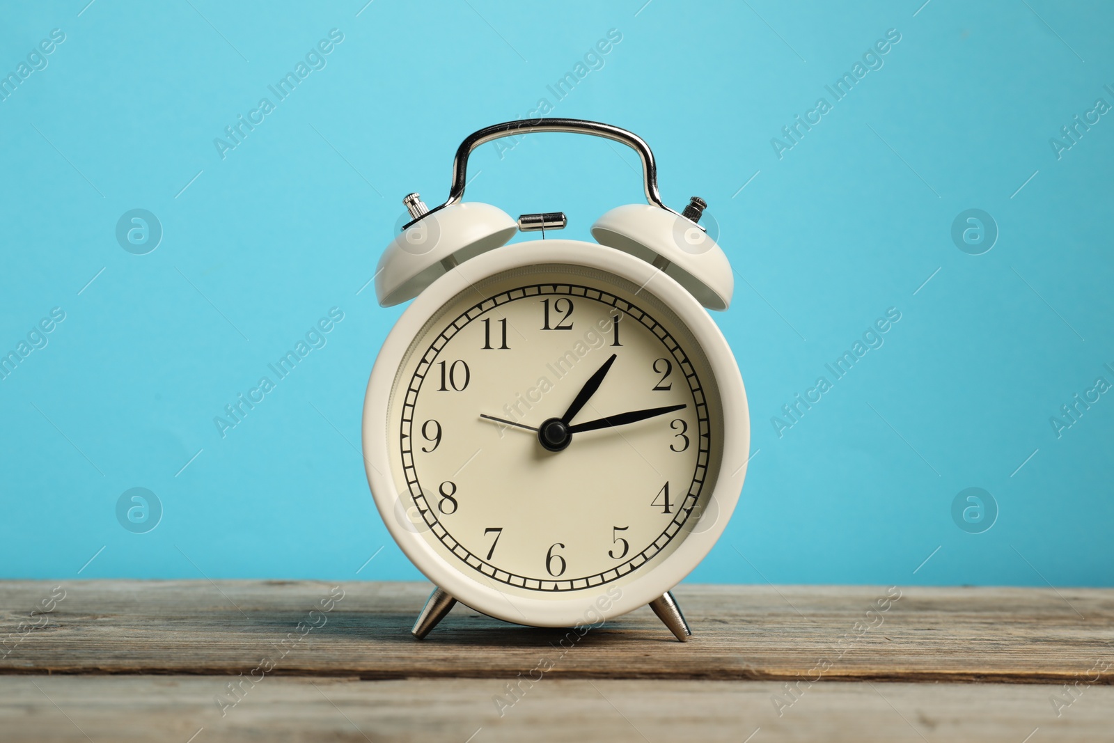 Photo of One white alarm clock on wooden table against light blue background