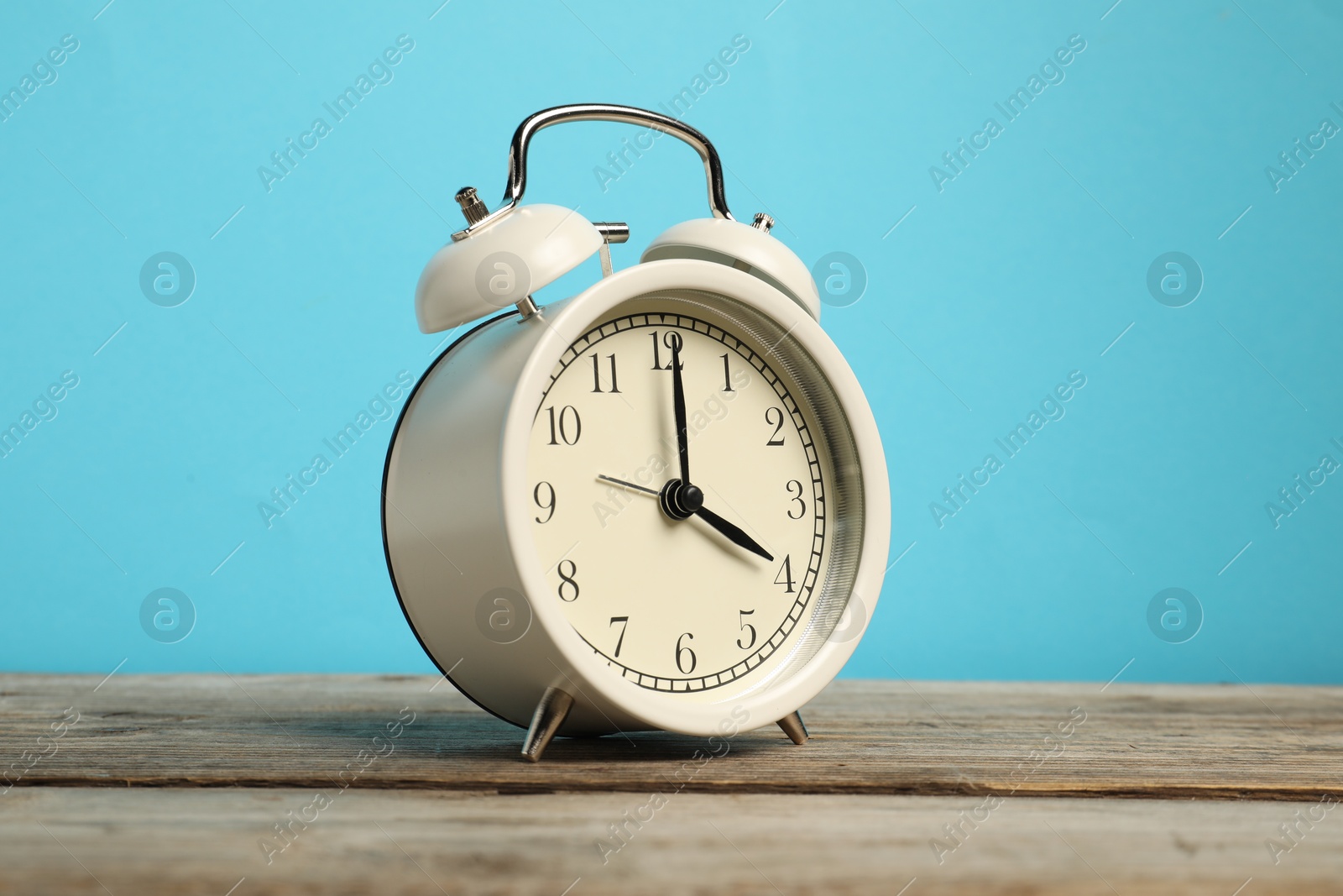 Photo of One white alarm clock on wooden table against light blue background