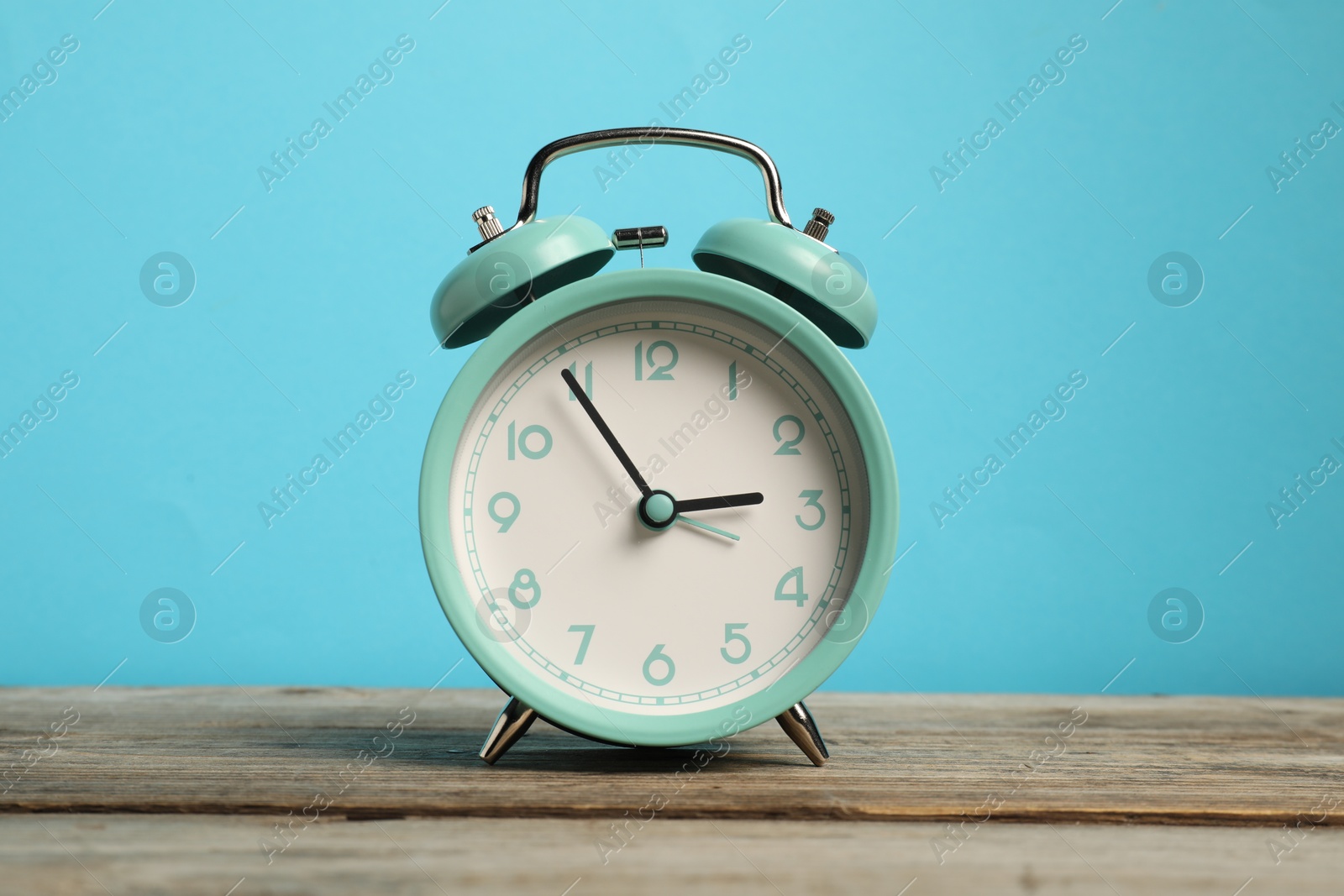 Photo of One turquoise alarm clock on wooden table against light blue background