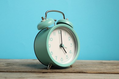 Photo of One turquoise alarm clock on wooden table against light blue background