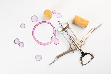 Photo of Wing corkscrew, corks and red wine stains on white background, top view