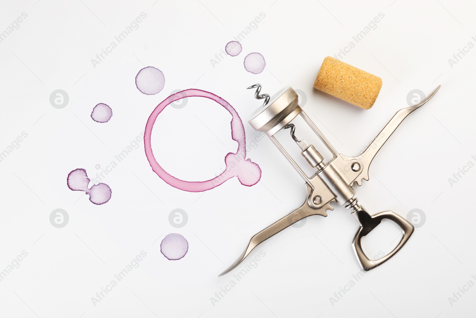 Photo of Wing corkscrew, cork and red wine stains on white background, top view