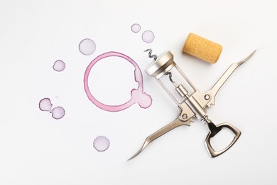 Photo of Wing corkscrew, cork and red wine stains on white background, top view