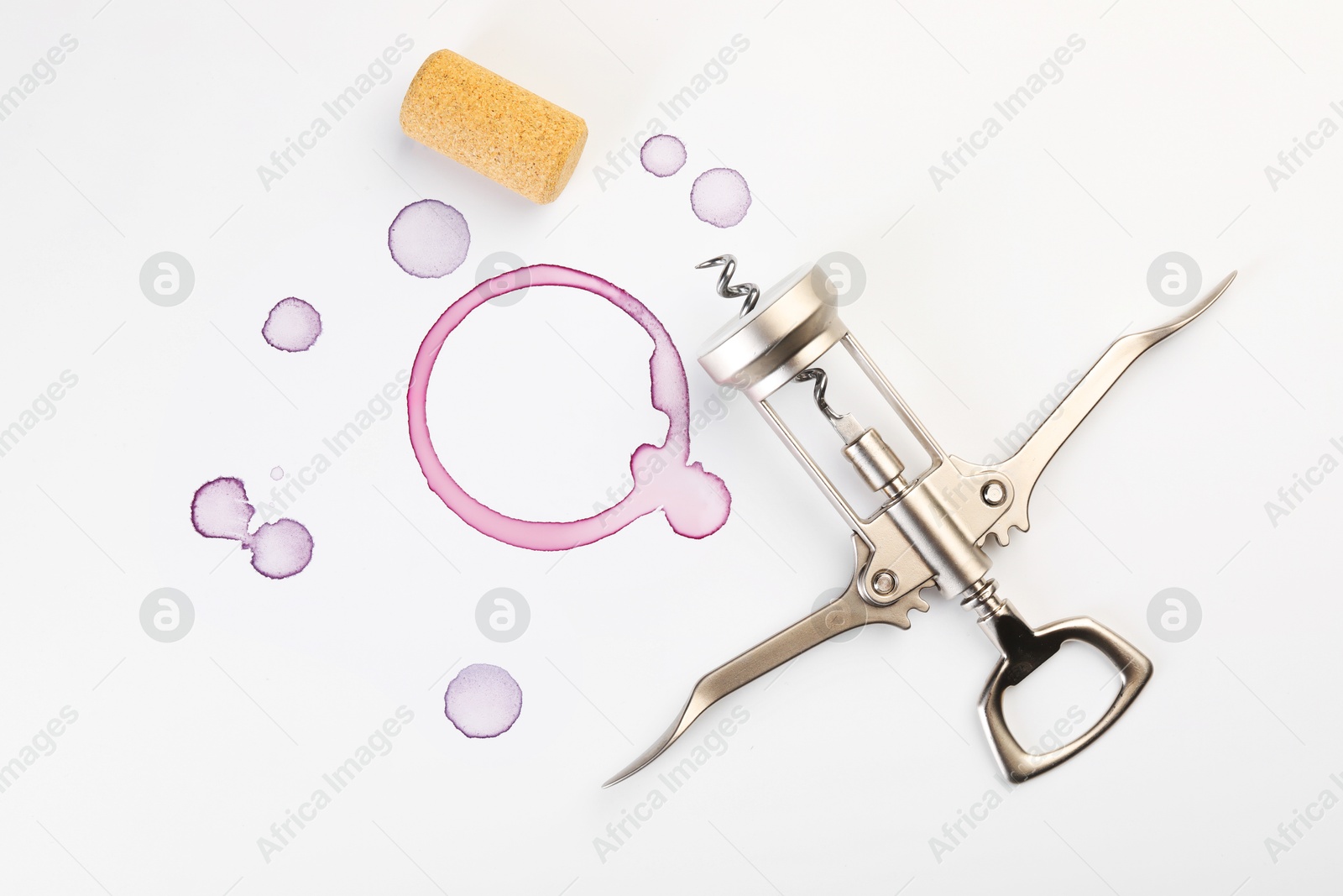 Photo of Wing corkscrew, cork and red wine stains on white background, top view