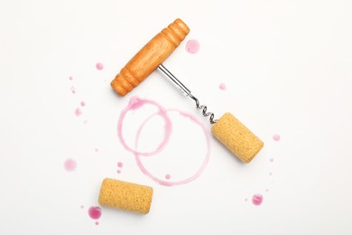 Photo of Corkscrew, corks and red wine stains on white background, top view