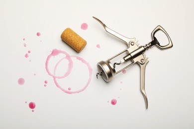 Photo of Wing corkscrew, cork and red wine stains on white background, top view