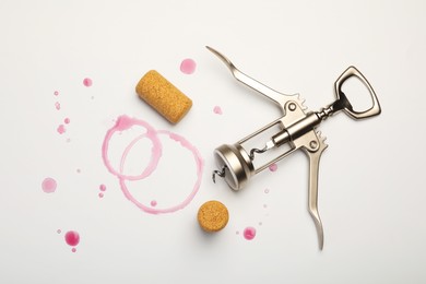 Photo of Wing corkscrew, corks and red wine stains on white background, top view