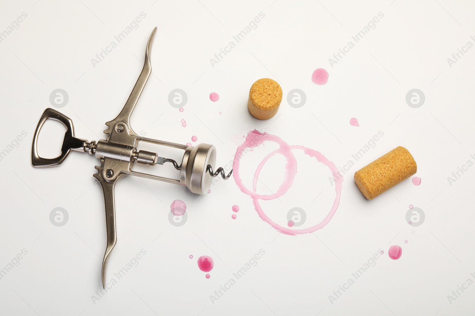 Photo of Wing corkscrew, corks and red wine stains on white background, top view