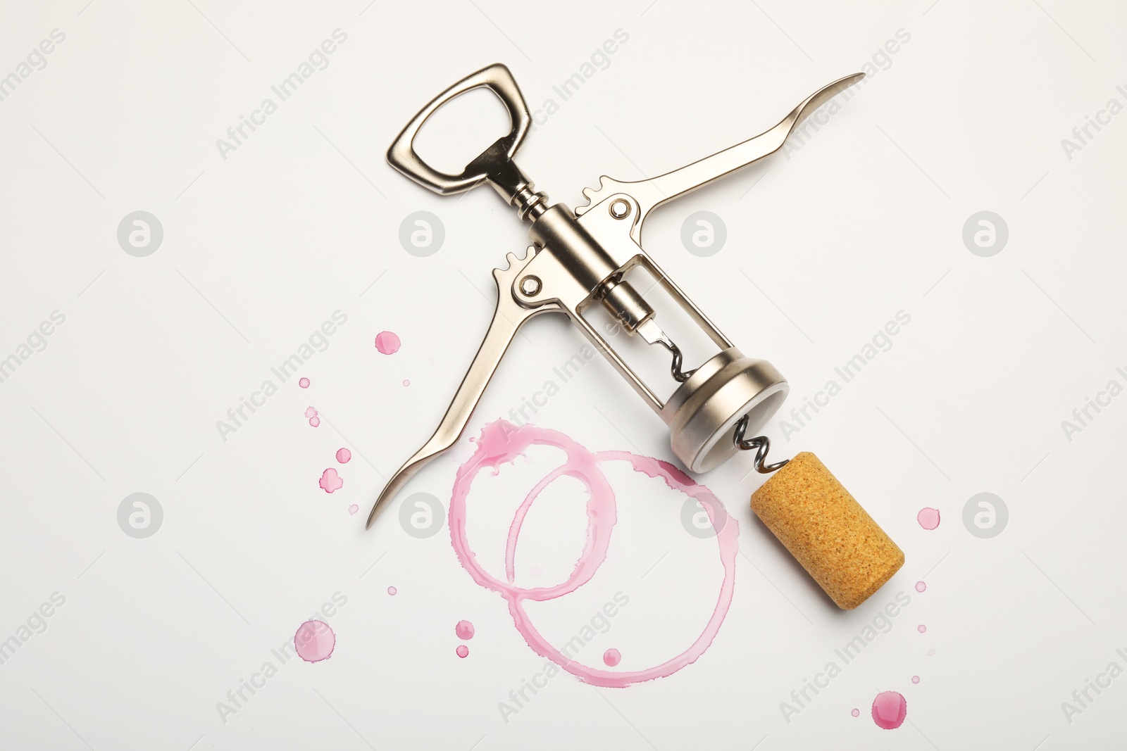 Photo of Wing corkscrew, cork and red wine stains on white background, top view