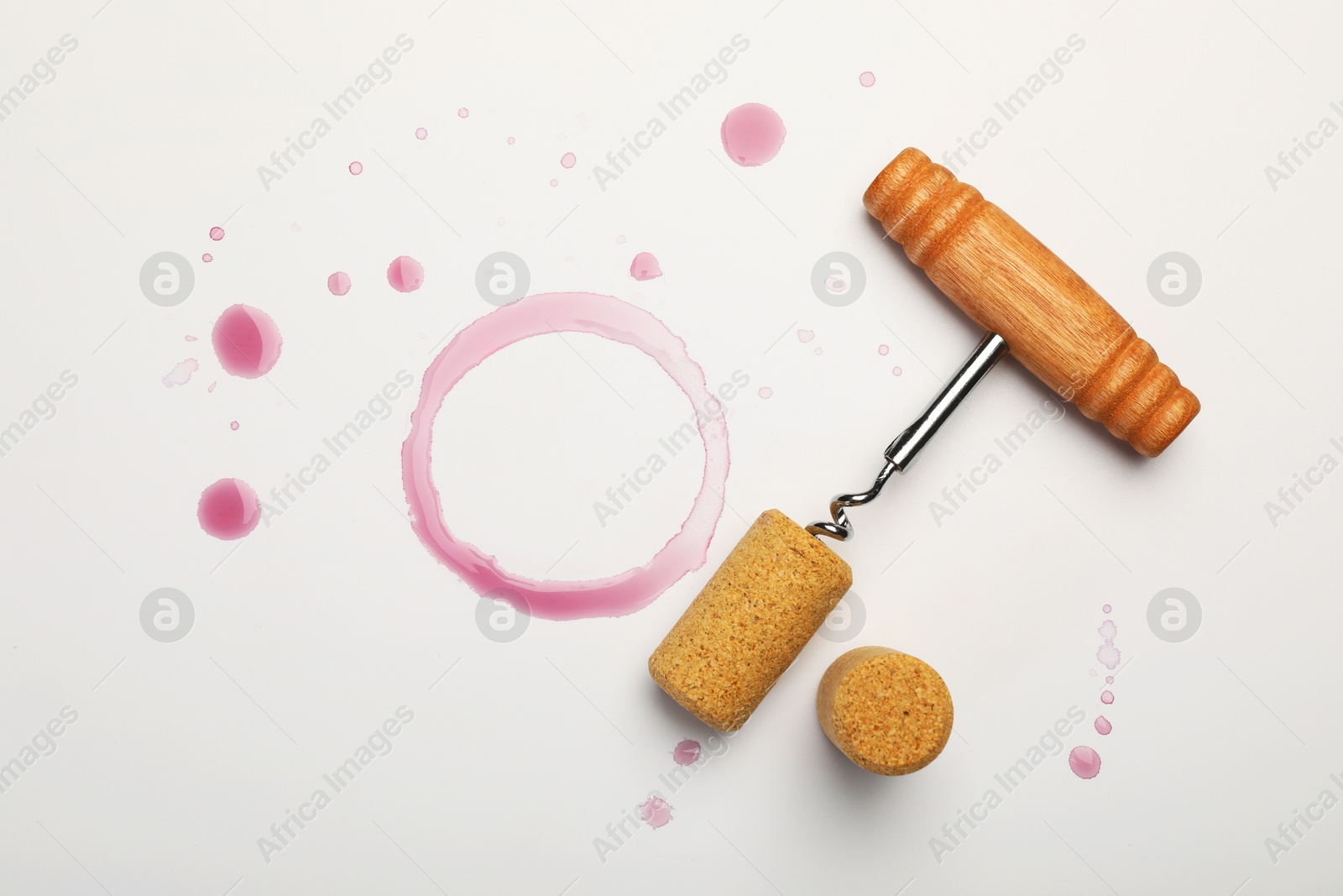 Photo of Corkscrew, corks and red wine stains on white background, top view