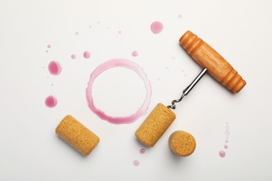 Photo of Corkscrew, corks and red wine stains on white background, top view