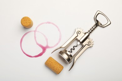 Photo of Wing corkscrew, corks and red wine stains on white background, top view