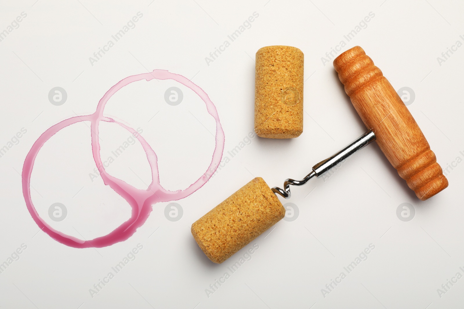 Photo of Corkscrew, corks and red wine stains on white background, top view