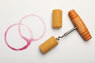 Photo of Corkscrew, corks and red wine stains on white background, top view