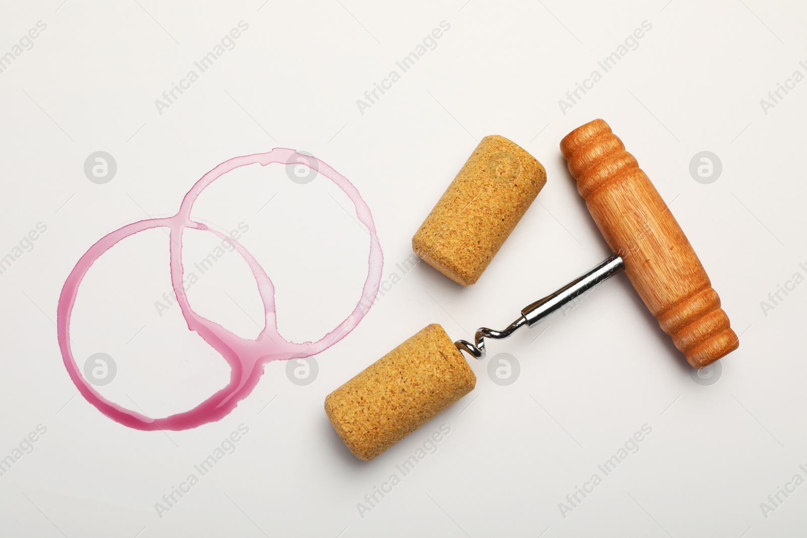 Photo of Corkscrew, corks and red wine stains on white background, top view