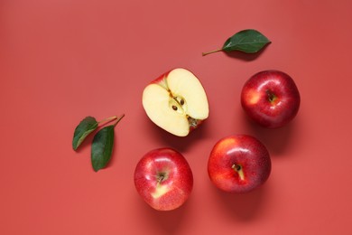 Photo of Fresh apples and green leaves on red background, flat lay