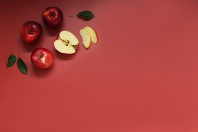 Photo of Fresh apples and green leaves on red background, flat lay. Space for text