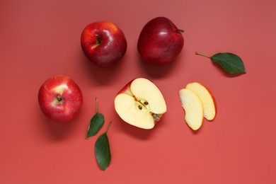 Photo of Fresh apples and green leaves on red background, flat lay