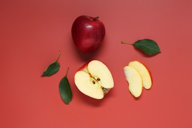 Photo of Fresh apples and green leaves on red background, flat lay