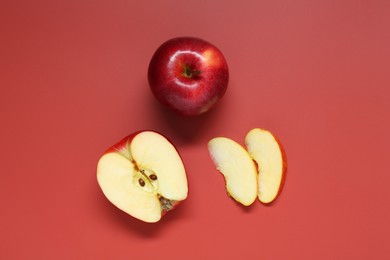 Photo of Whole and cut apples on red background, flat lay