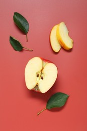 Photo of Cut apple and green leaves on red background, flat lay