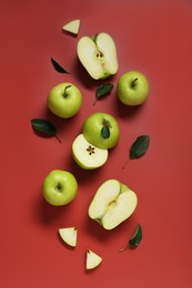 Photo of Fresh apples and green leaves on red background, flat lay