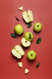 Photo of Fresh apples and green leaves on red background, flat lay