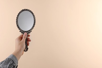 Woman holding beautiful mirror on beige background, closeup. Space for text