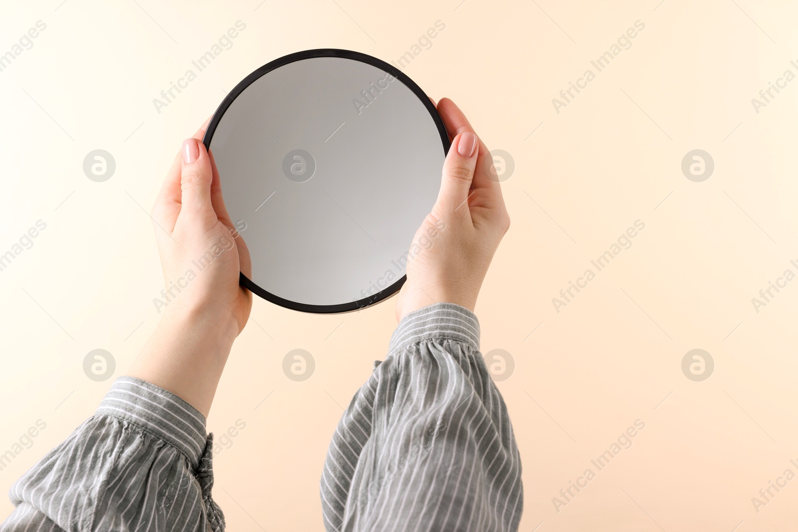 Photo of Woman holding round mirror on beige background, closeup