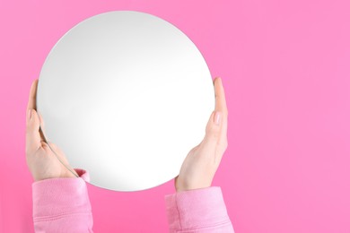 Photo of Woman holding round mirror on pink background, closeup. Space for text