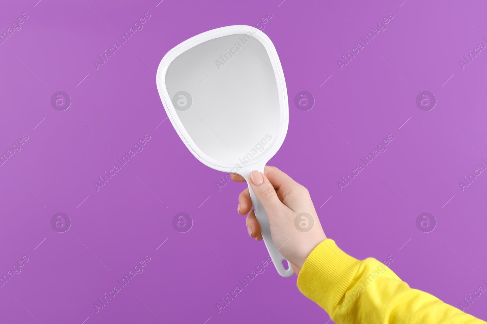 Photo of Woman holding handheld mirror on violet background, closeup