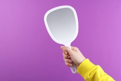 Photo of Woman holding handheld mirror on violet background, closeup. Space for text