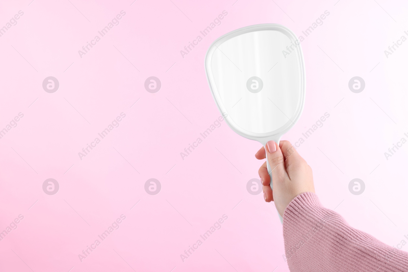 Photo of Woman holding handheld mirror on pink background, closeup. Space for text