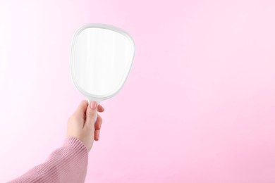 Photo of Woman holding handheld mirror on pink background, closeup. Space for text