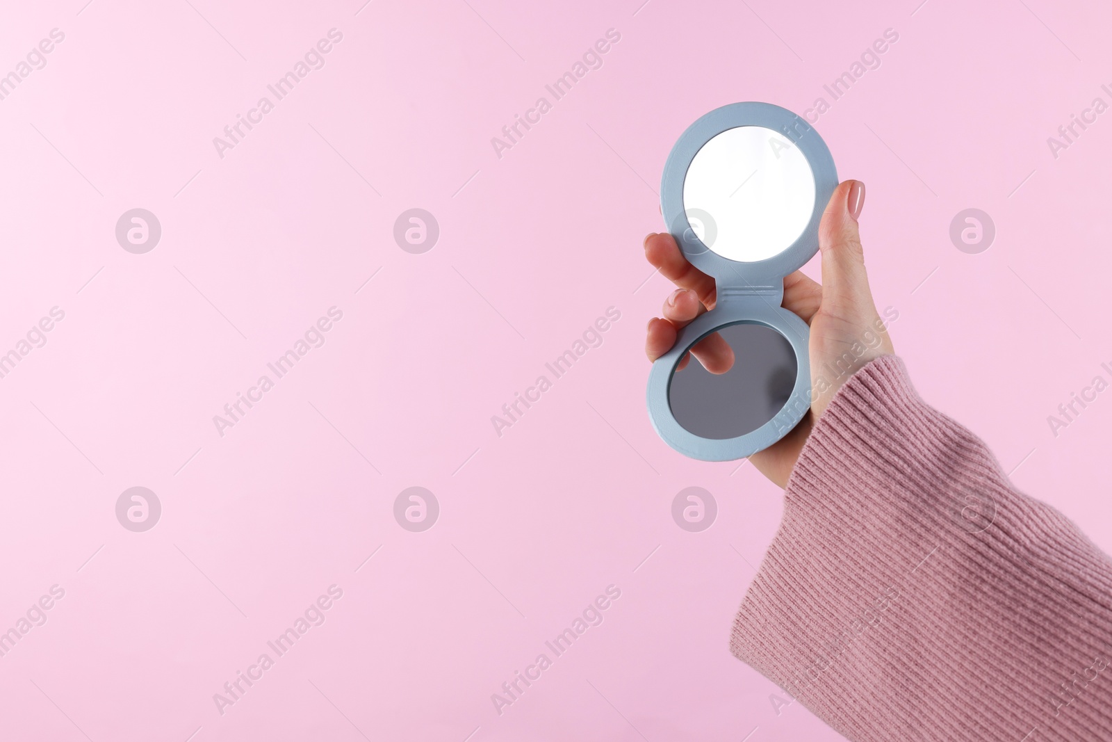 Photo of Woman holding pocket mirror on pink background, closeup. Space for text