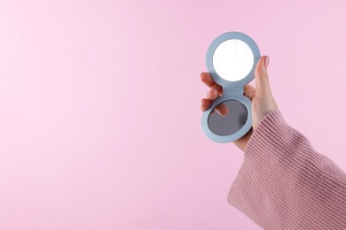 Photo of Woman holding pocket mirror on pink background, closeup. Space for text