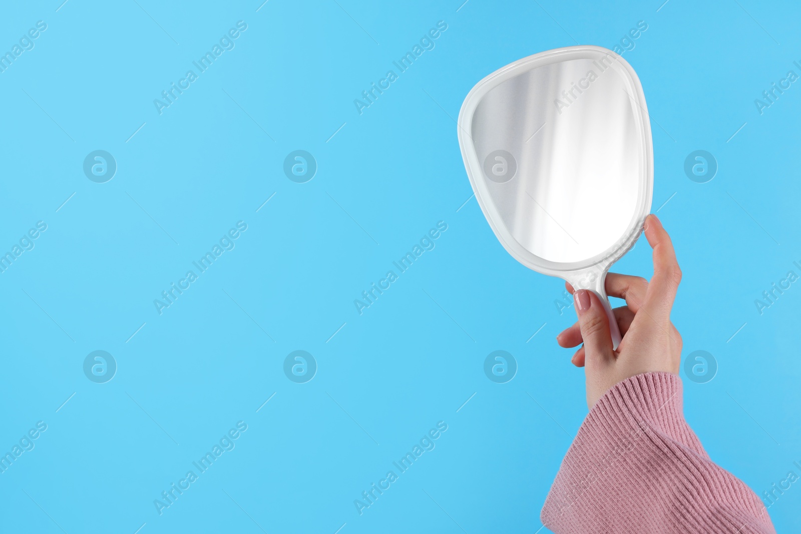 Photo of Woman holding handheld mirror on light blue background, closeup. Space for text