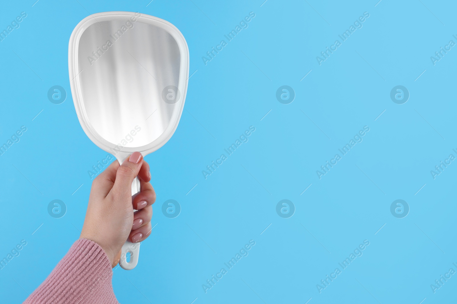 Photo of Woman holding handheld mirror on light blue background, closeup. Space for text