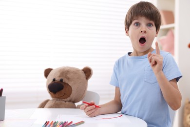 Photo of Emotional boy had idea for his drawing at white table in kindergarten