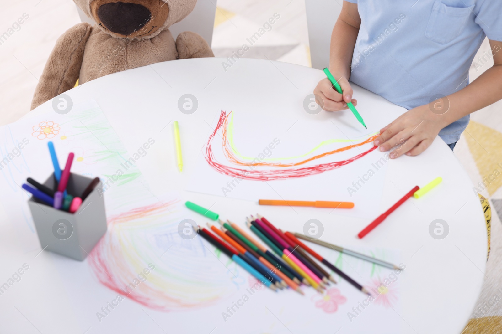 Photo of Boy drawing rainbow at white table indoors, closeup